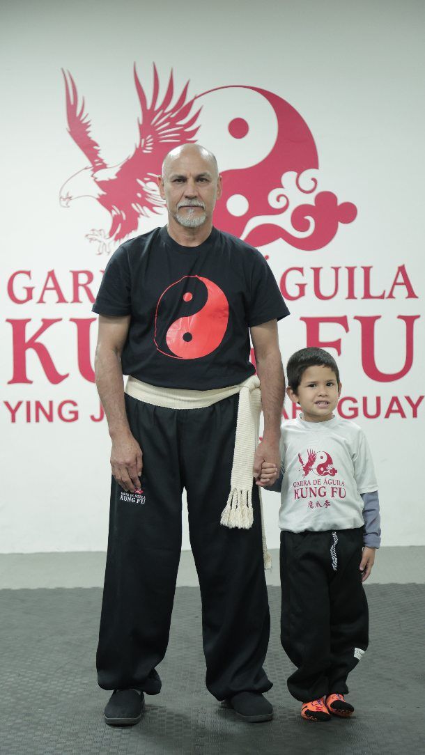 El Sifu y un alumno pequeño posan frente al emblema de la academia
